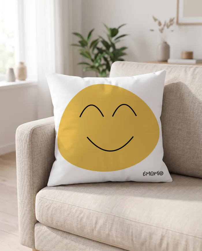 Le coussin Émomio de la joie, visage jaune souriant, posé dans l'angle d'un canapé.